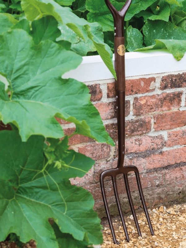 Garden fork leaning against a brick wall in a garden setting