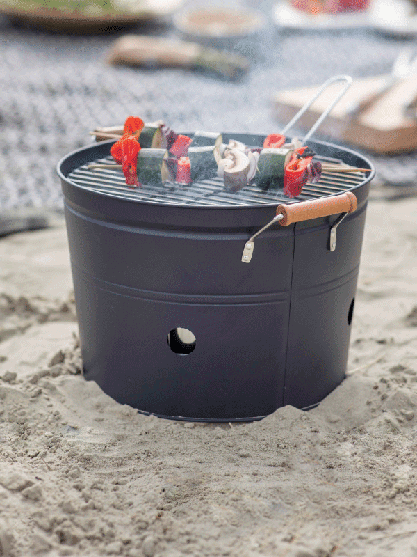 Black bucket BBQ on the beach with vegetable skewers grilling