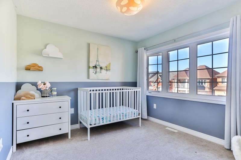 A bright and clean nursery with cloud decorations and a white cot