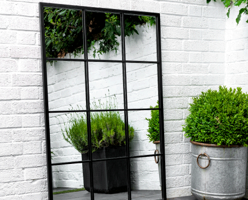 A stylish outdoor mirror reflecting plant pots while leaning against a white wall