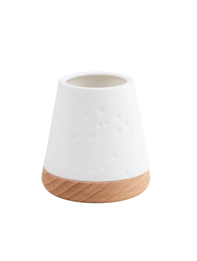 White unglazed porcelain tealight holder with embossed dots on an oiled wooden base by Räder, casting a warm glow when lit.