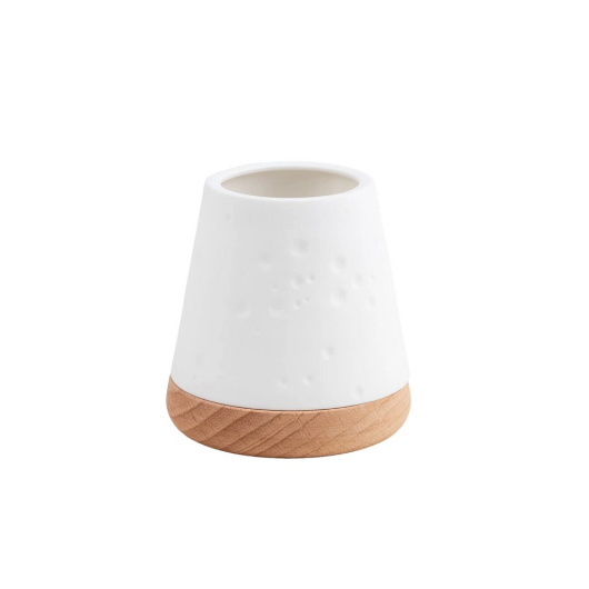 White unglazed porcelain tealight holder with embossed dots on an oiled wooden base by Räder, casting a warm glow when lit.