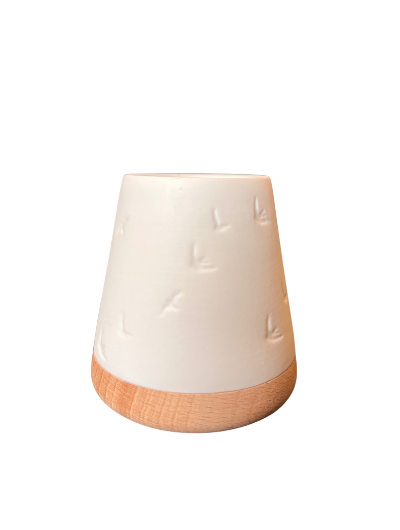 White unglazed porcelain tealight holder with embossed birds on an oiled wooden base by Räder, casting a warm glow when lit.