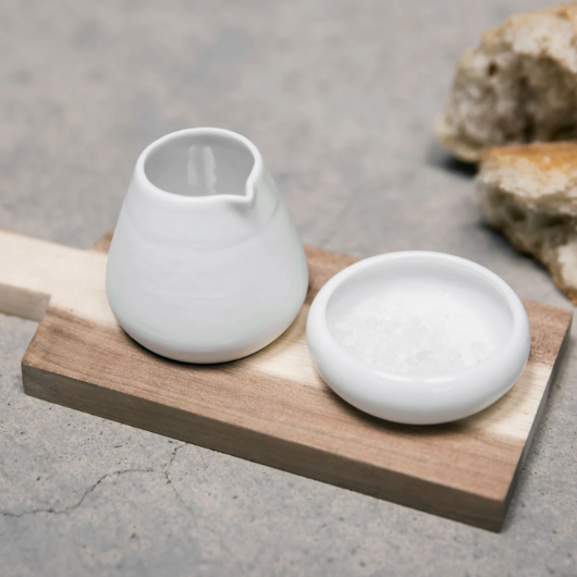 Oil and salt pots with acacia wood tray by Räder Designs, porcelain vessels by Indigo Ruh, versatile for oils, spices, or condiments.