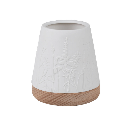 White unglazed porcelain tealight holder with embossed flowers on an oiled wooden base by Räder, casting a warm glow when lit.