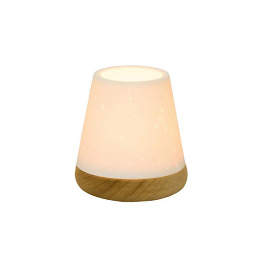 White unglazed porcelain tealight holder with embossed dots on an oiled wooden base by Räder, casting a warm glow when lit.