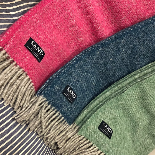 Sand Cornwall ink-blue pure new wool blanket with cream tassels and soft textured weave, draped over a sofa.