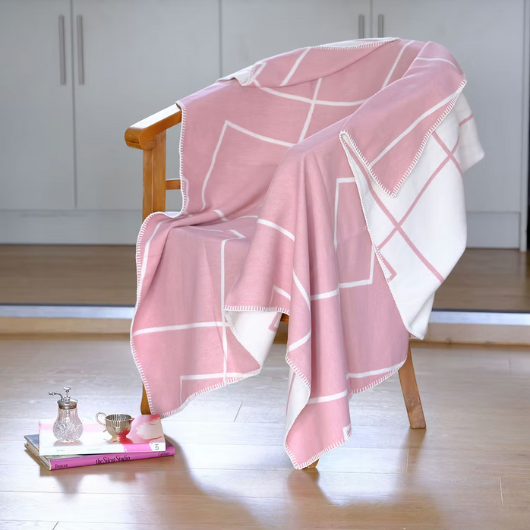 Geometric Pink Organic Cotton Blanket Throw with white pattern and blanket stitch edge, displayed folded on a bed.