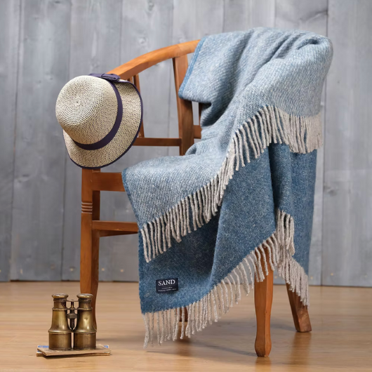 Sand Cornwall ink-blue pure new wool blanket with cream tassels and soft textured weave, draped over a sofa.