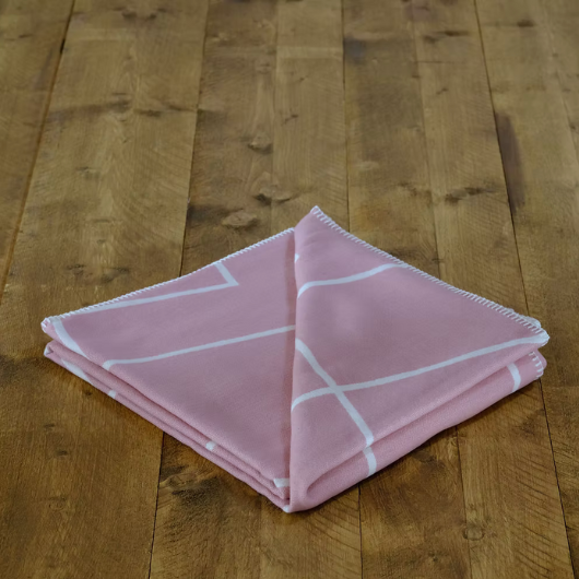 Geometric Pink Organic Cotton Blanket Throw with white pattern and blanket stitch edge, displayed folded on a bed.