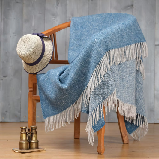 Sand Cornwall ink-blue pure new wool blanket with cream tassels and soft textured weave, draped over a sofa.