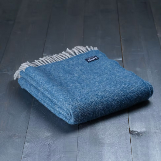 Sand Cornwall ink-blue pure new wool blanket with cream tassels and soft textured weave, draped over a sofa.