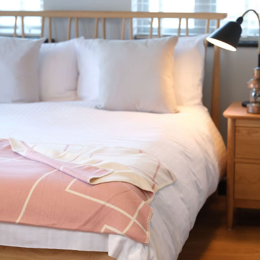 Geometric Pink Organic Cotton Blanket Throw with white pattern and blanket stitch edge, displayed folded on a bed.