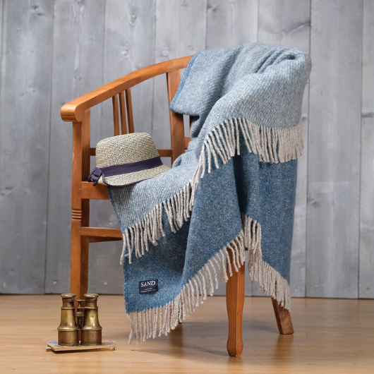Sand Cornwall ink-blue pure new wool blanket with cream tassels and soft textured weave, draped over a sofa.