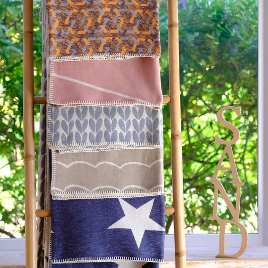 Geometric Pink Organic Cotton Blanket Throw with white pattern and blanket stitch edge, displayed folded on a bed.