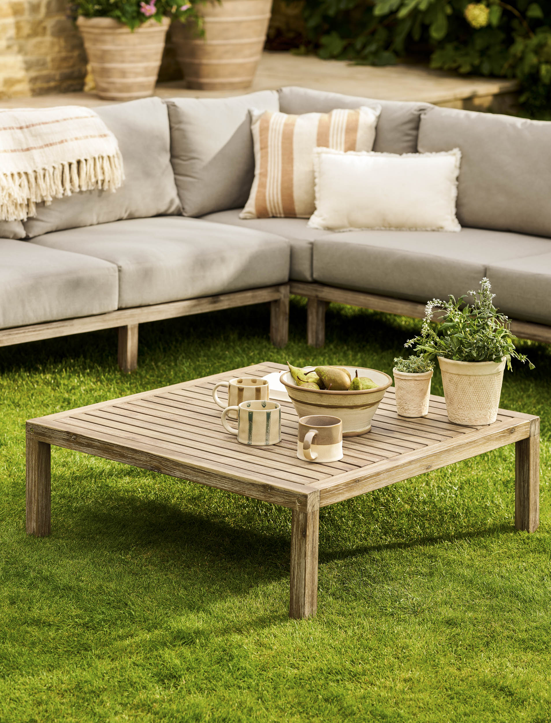 Garden Trading Porthallow Dark Natural acacia corner sofa set with matching armchair and coffee table on a garden patio.