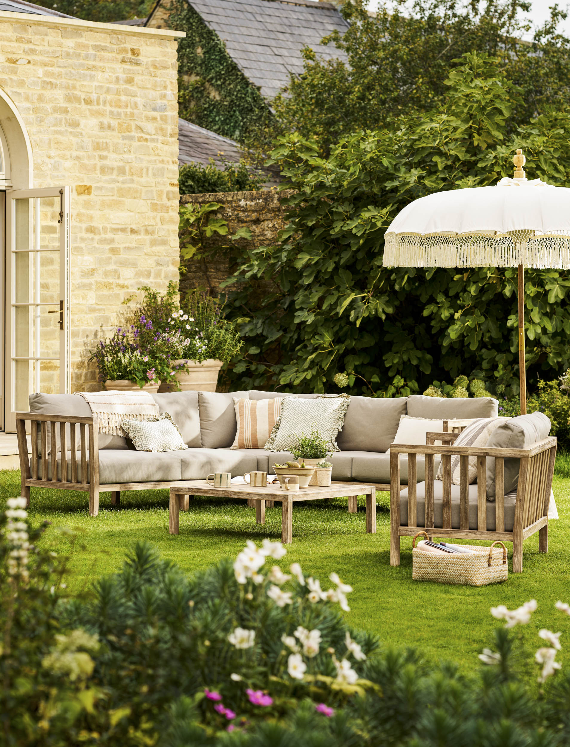 Garden Trading Porthallow Dark Natural acacia corner sofa set with matching armchair and coffee table on a garden patio.
