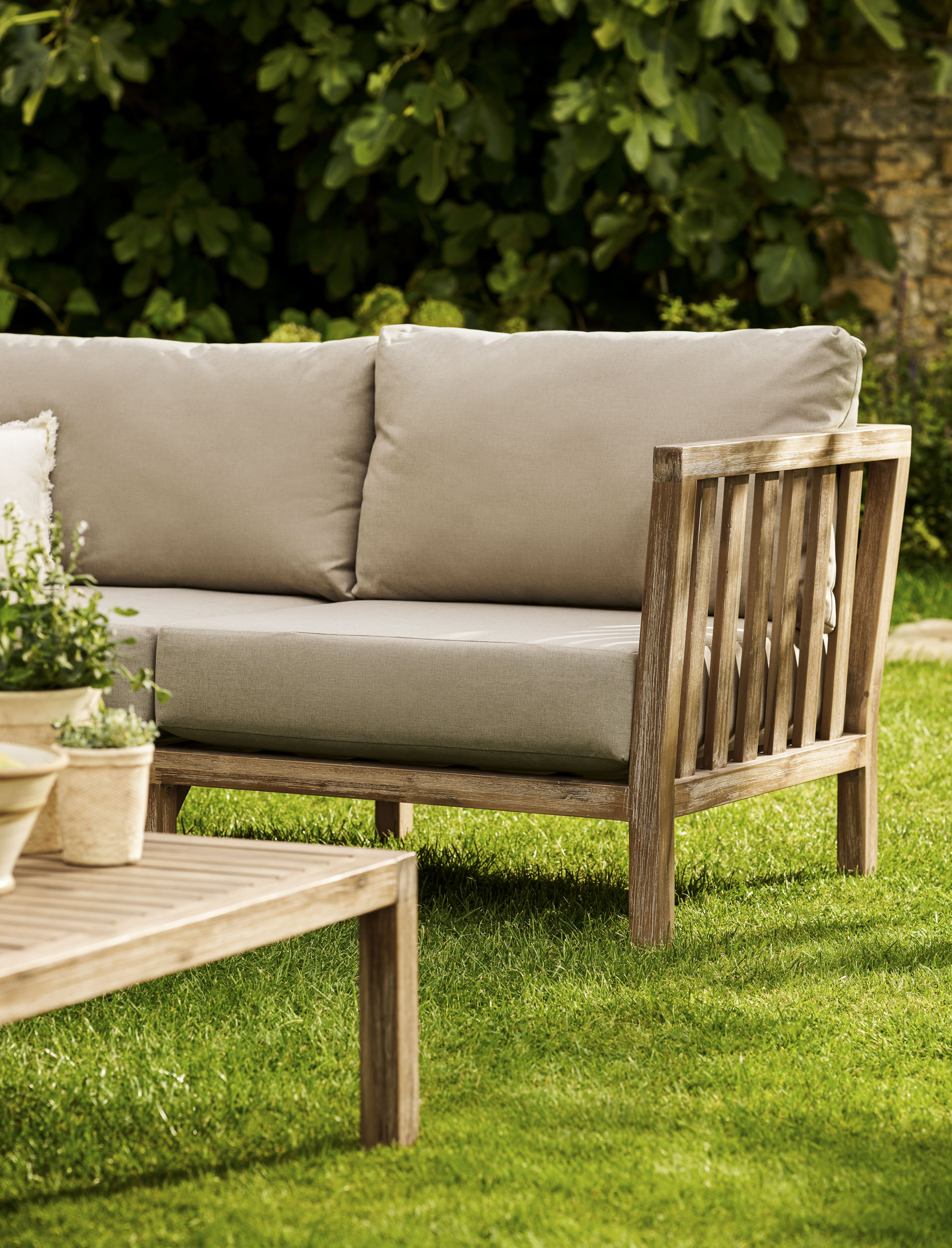 Garden Trading Porthallow Dark Natural acacia corner sofa set with matching armchair and coffee table on a garden patio. Sizes