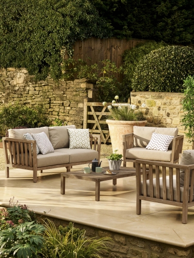 Garden Trading Porthallow 2 seater sofa set in dark natural acacia wood with matching armchairs and coffee table on a patio.
