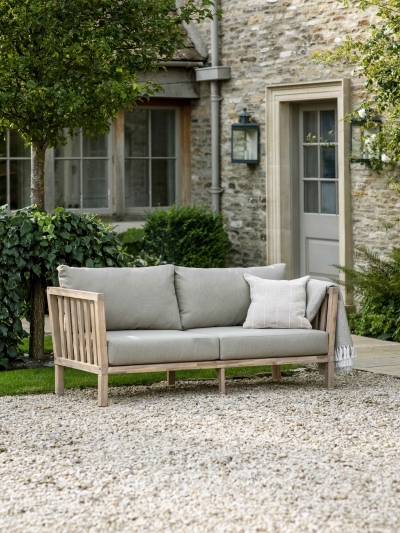 Garden Trading Porthallow 2 seater sofa in natural acacia wood with grey cushions styled on an outdoor patio.
