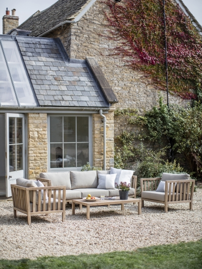 Garden Trading Porthallow 3 seater sofa set in natural acacia wood with grey cushions, armchairs and coffee table on a patio.