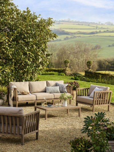 Garden Trading Porthallow 3 seater sofa set in dark natural acacia wood with matching armchairs and coffee table on a patio.