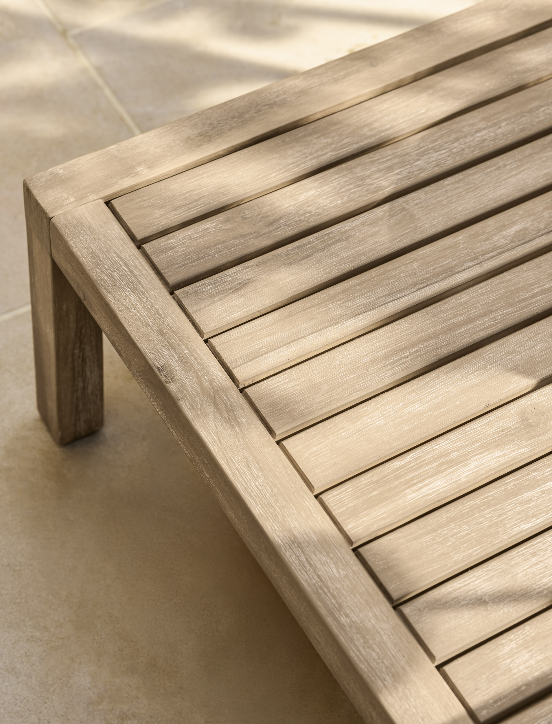 Garden Trading Porthallow 2 seater sofa set in natural acacia wood with matching armchairs and coffee table outdoors.