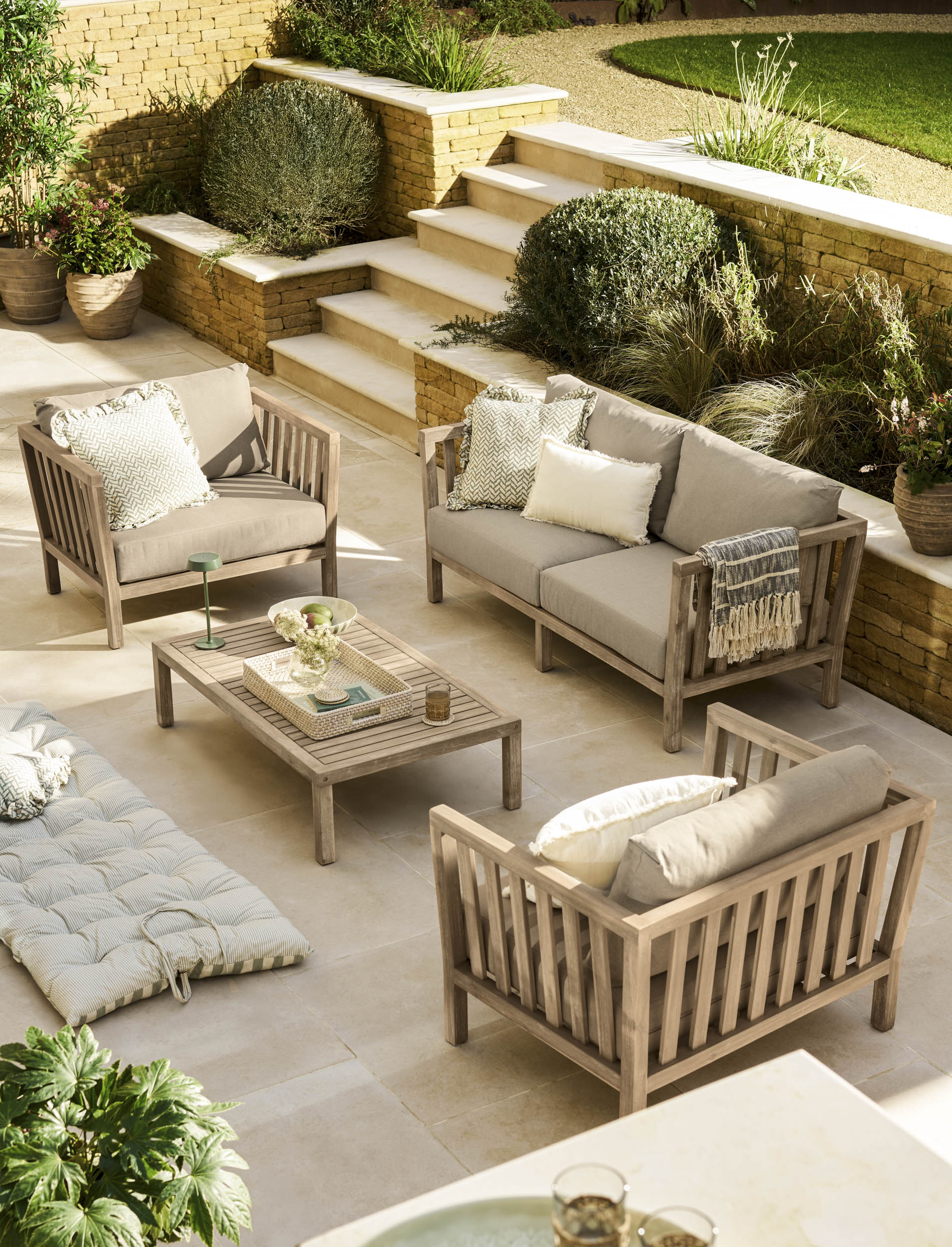 Garden Trading Porthallow 2 seater sofa set in natural acacia wood with matching armchairs and coffee table outdoors.