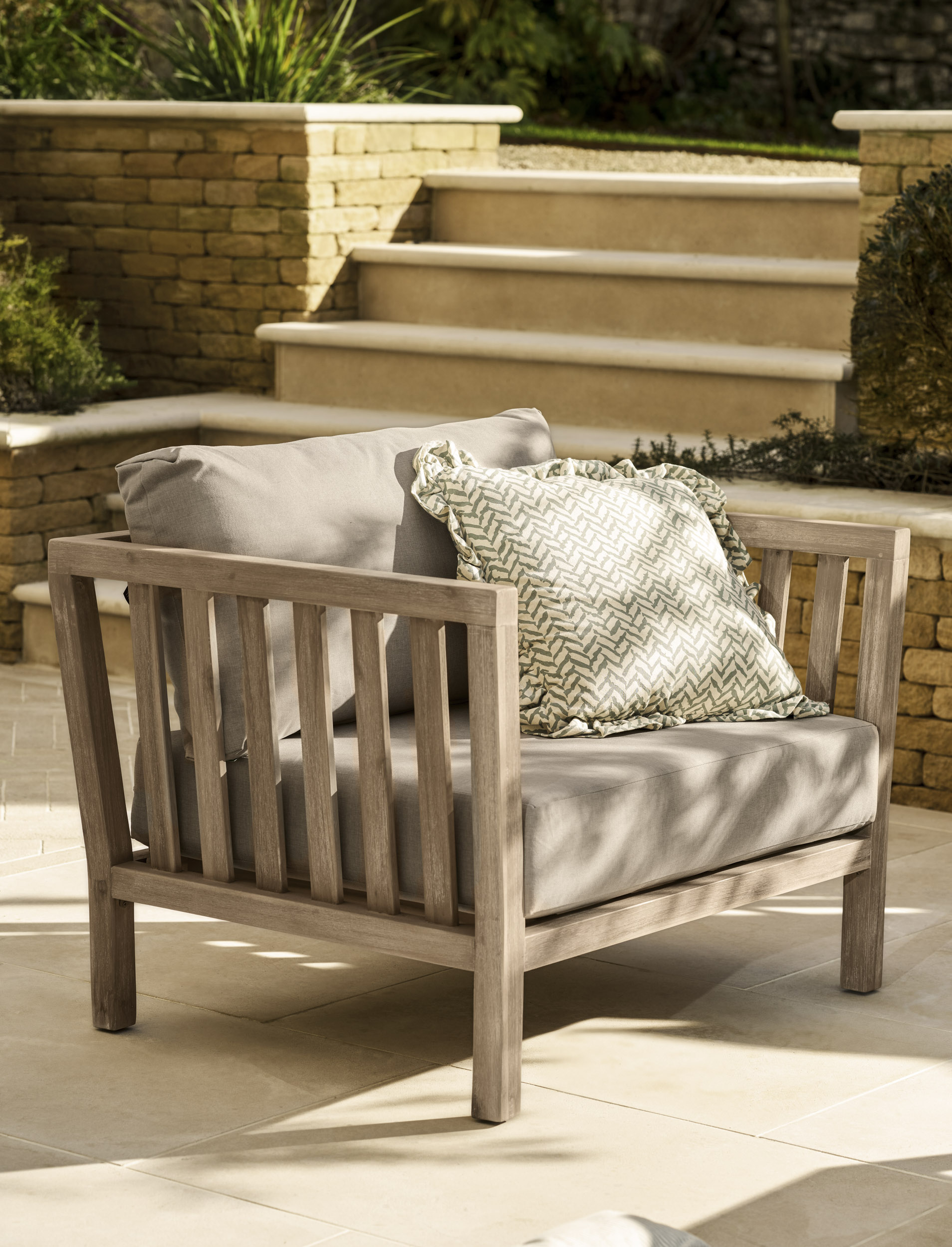 Garden Trading Porthallow 2 seater sofa set in natural acacia wood with matching armchairs and coffee table outdoors.