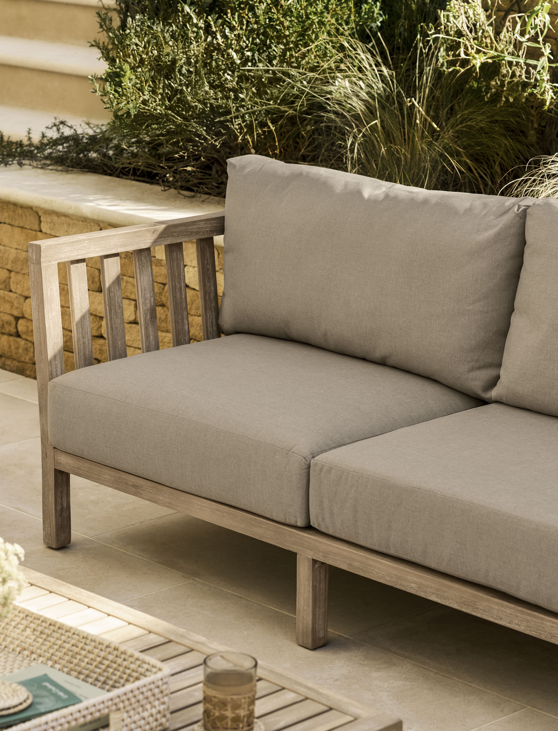 Garden Trading Porthallow 2 seater sofa set in natural acacia wood with matching armchairs and coffee table outdoors.