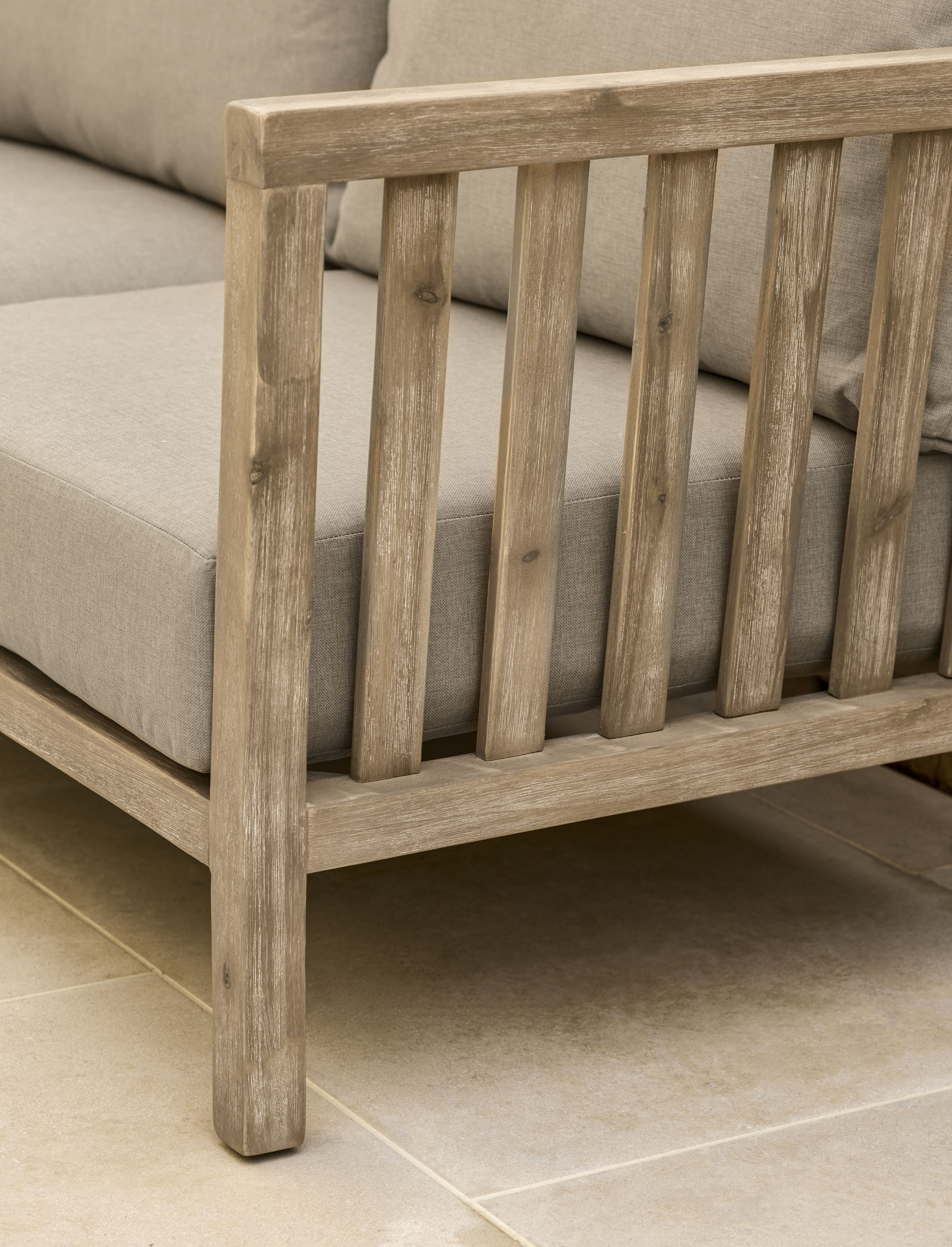 Garden Trading Porthallow 2 seater sofa set in natural acacia wood with matching armchairs and coffee table outdoors.