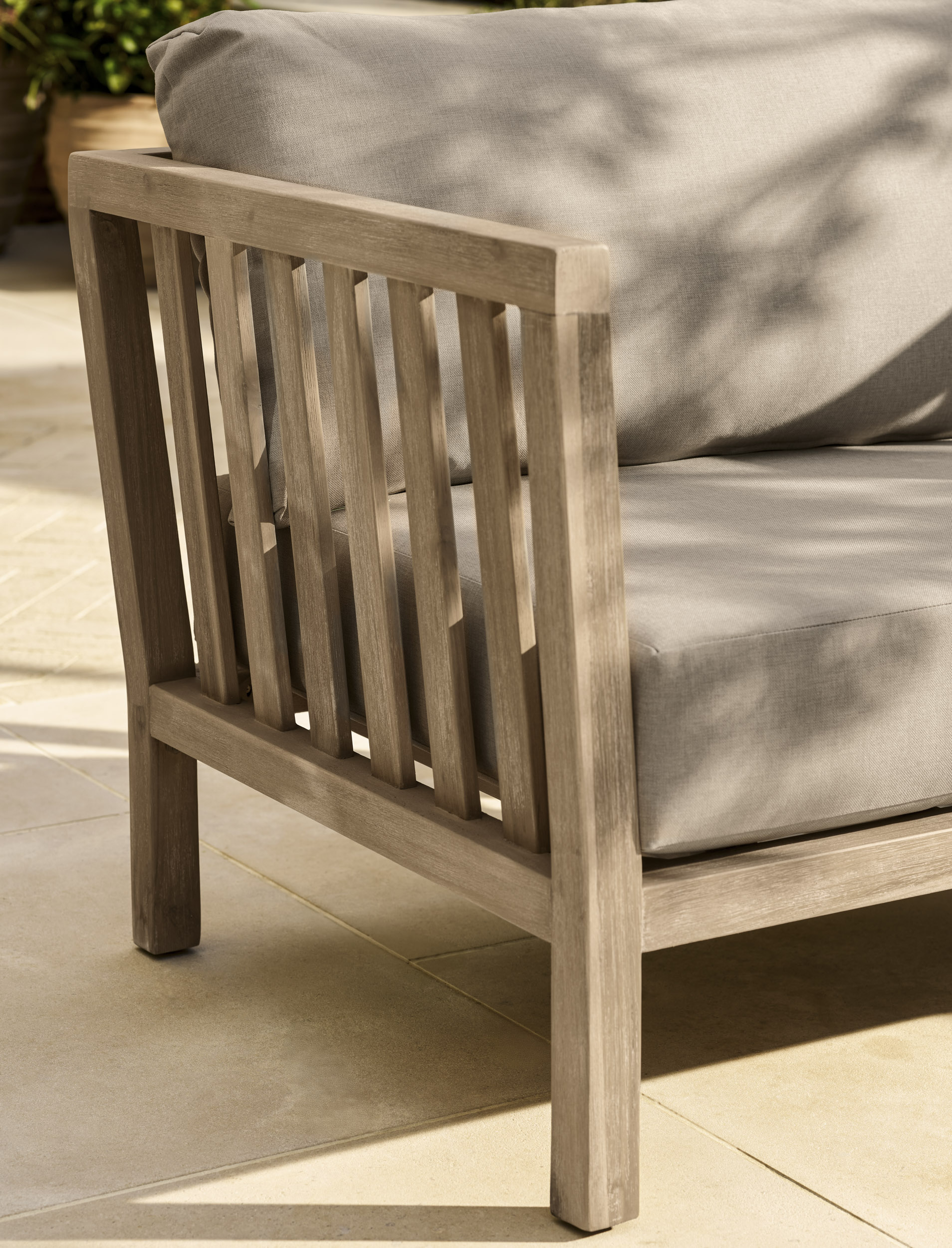 Garden Trading Porthallow 2 seater sofa set in natural acacia wood with matching armchairs and coffee table outdoors.